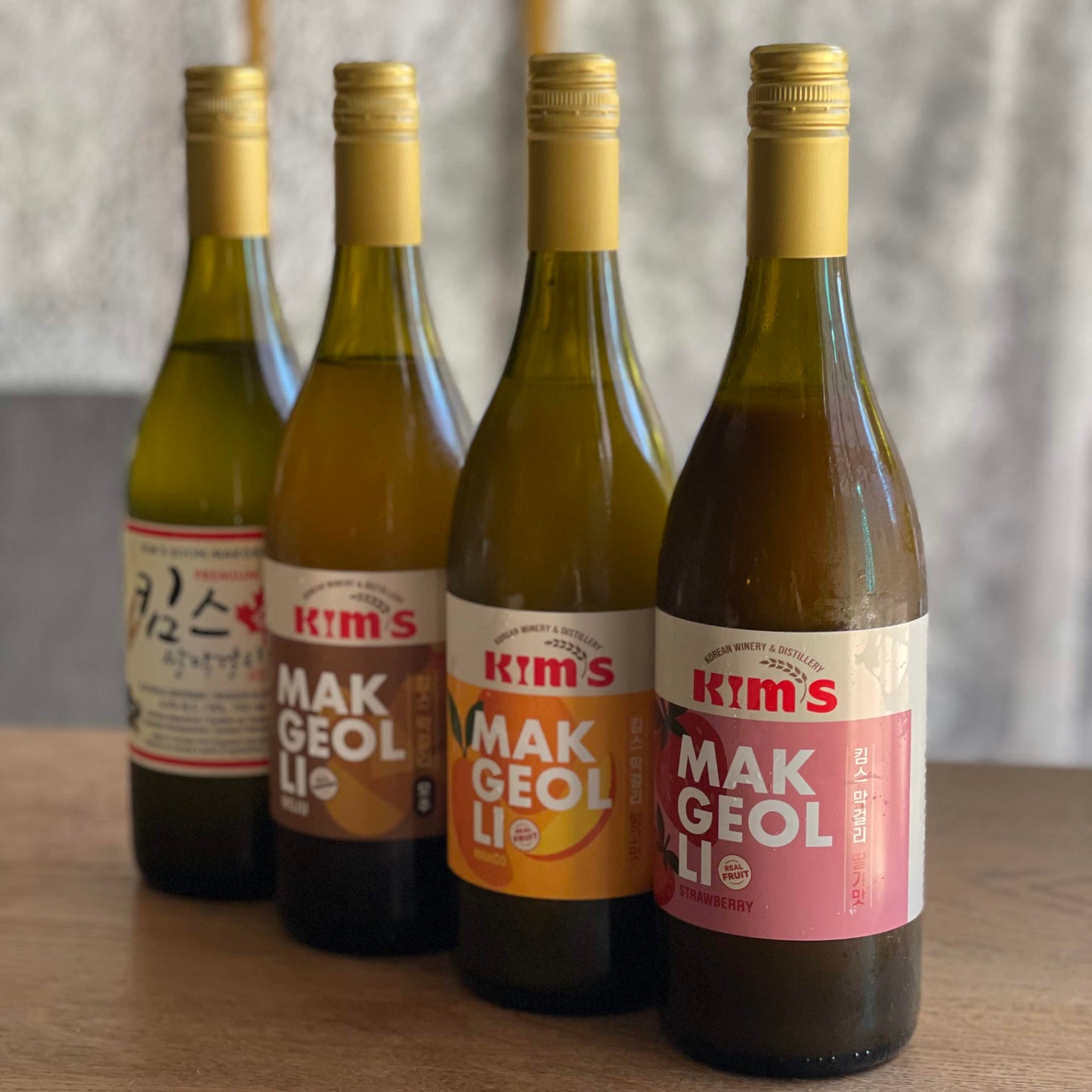 Four bottles of Kim's Makgeolli on a wooden surface with a blurred background.