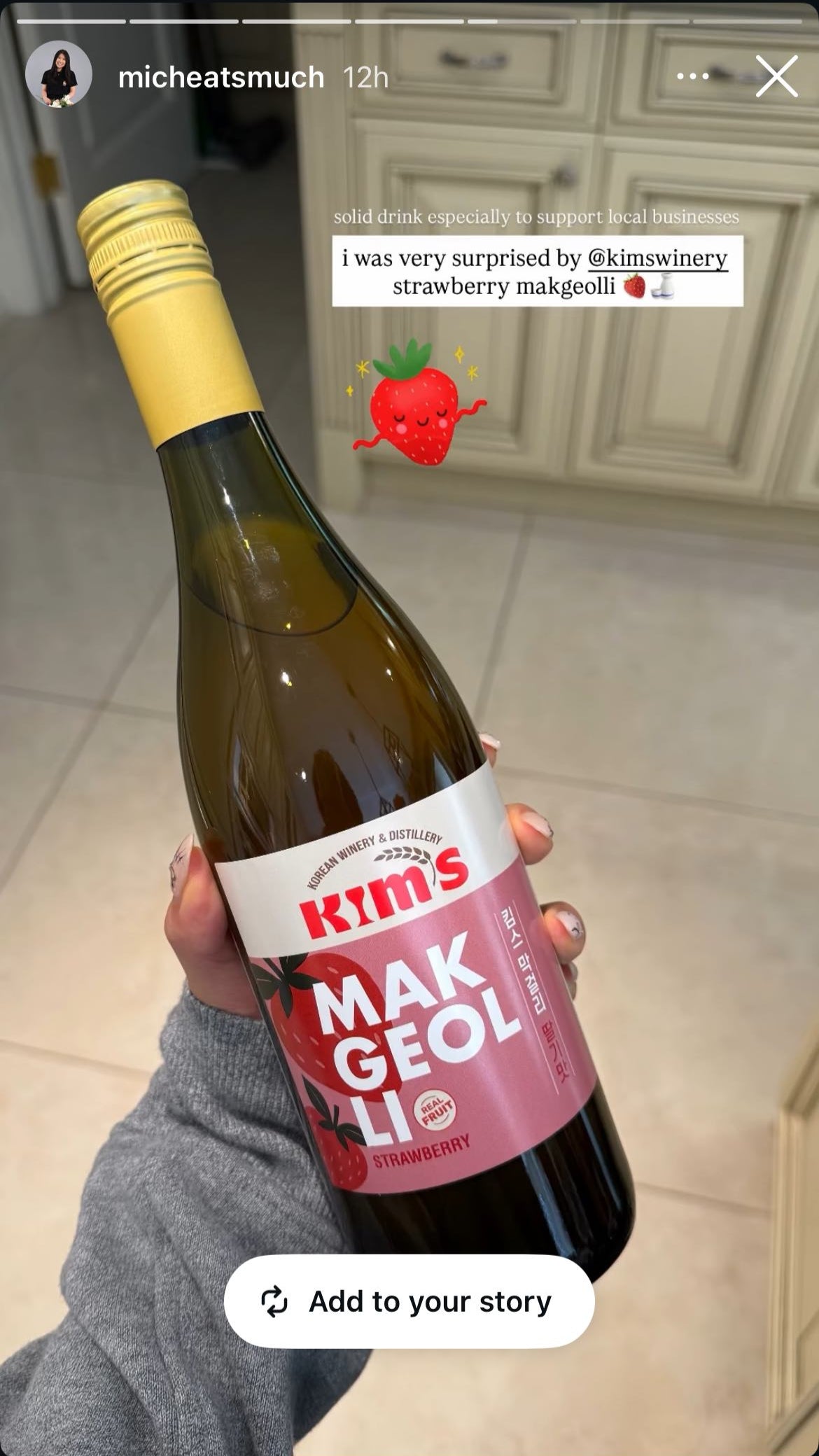 Bottle of Kim's Strawberry Makgeolli held by a person with a kitchen background, with a caption describing how good the strawberry makgeolli is.